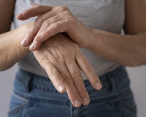 Eine Person hält eine Hand mit der anderen, die Hände sind leicht gefaltet und zeigen gepflegte Nägel.